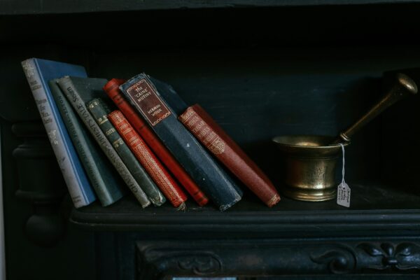 A collection of vintage books and a brass mortar on a dark shelf creates a classic still life scene.